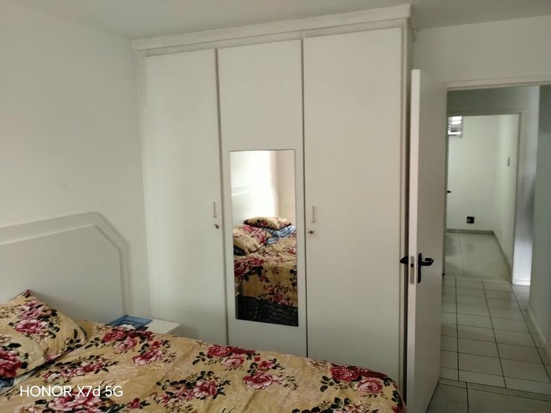 Bedroom featuring a white built-in wardrobe with a central mirrored panel and tiled flooring, leading into an adjacent hallway.