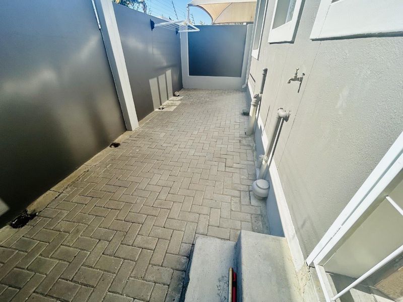 A paved outdoor utility area featuring a wall-mounted drying rack, external water tap, and secure boundary walls.