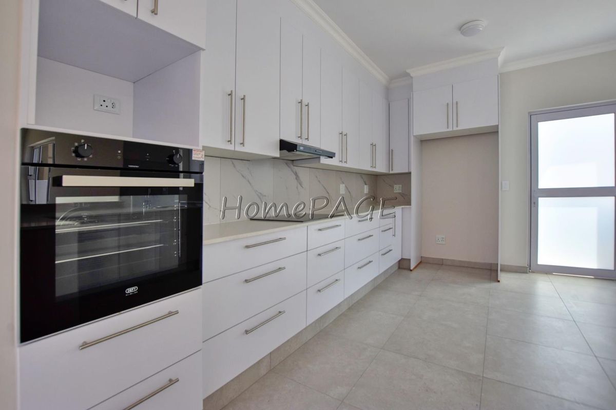 Modern kitchen featuring white cabinetry, marble-look splashback, built-in oven, extractor fan, and tiled flooring with direct access to the exterior.