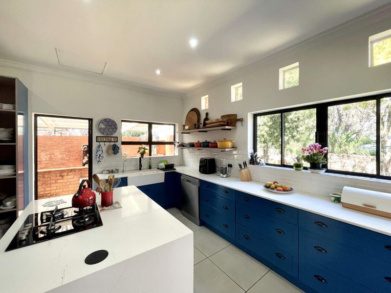 Modern kitchen featuring a central island with gas hob, farmhouse sink, blue cabinetry, stone countertops, and subway tile backsplash with ample natural light.
