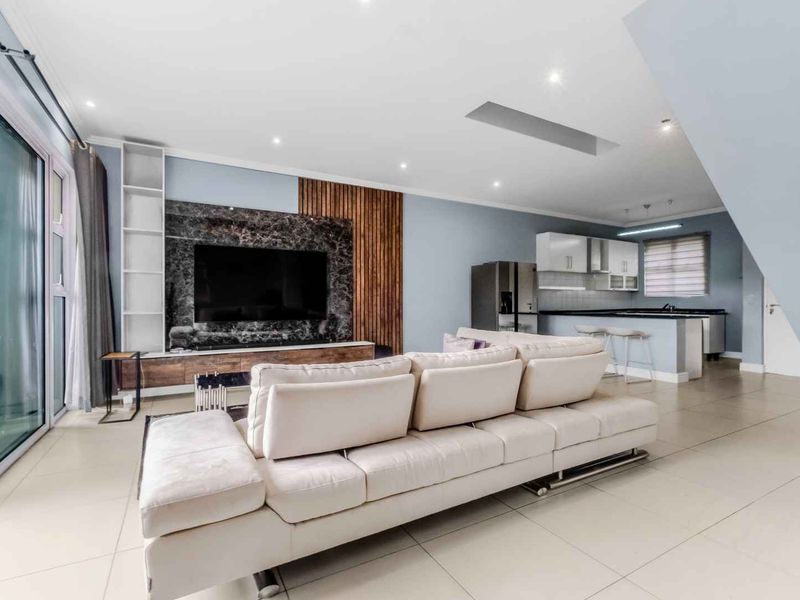 Modern open-plan living area featuring a marble media wall, timber accents, tiled floors, and a sleek kitchen with an island and stone countertops.