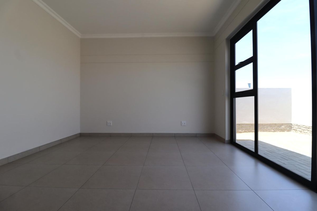 A bright, empty living room featuring neutral tiled flooring, modern black-framed sliding glass doors, and clean, minimalist wall finishes.