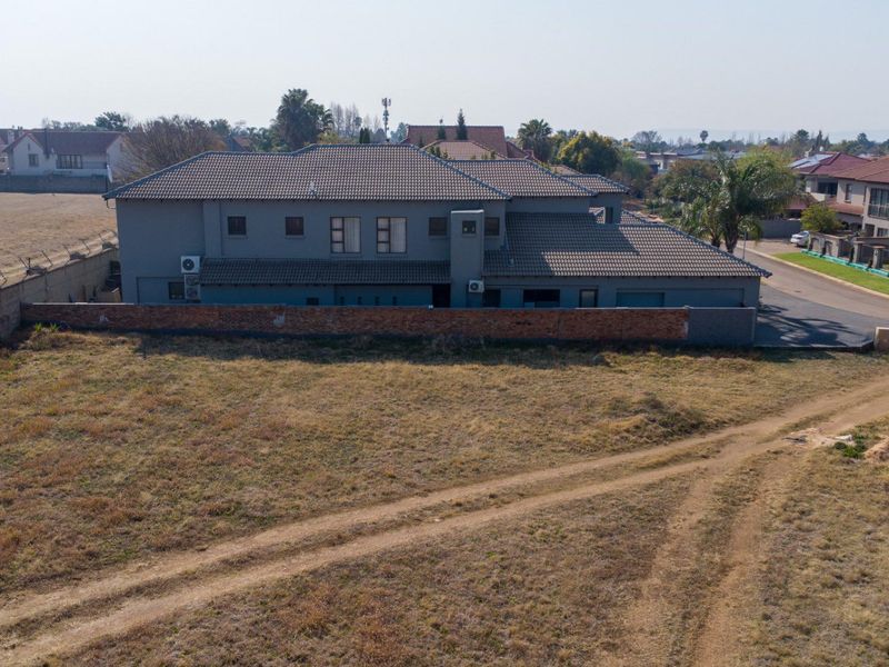 Aerial view of a residential property featuring a large vacant plot adjacent to a multi-story dwelling with a tiled roof and perimeter wall.