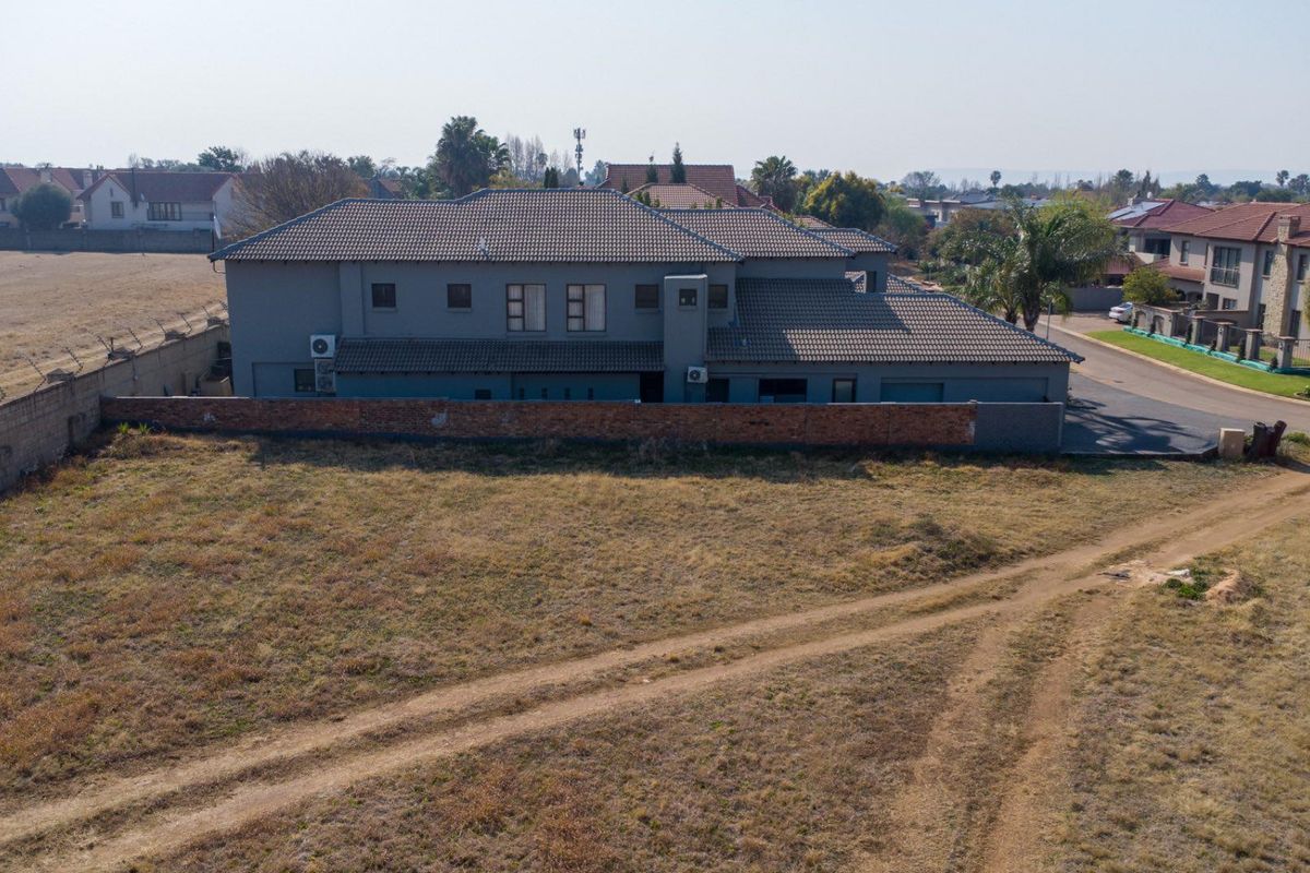 Aerial view of a residential property featuring a large vacant plot adjacent to a multi-story dwelling with a tiled roof and perimeter wall.