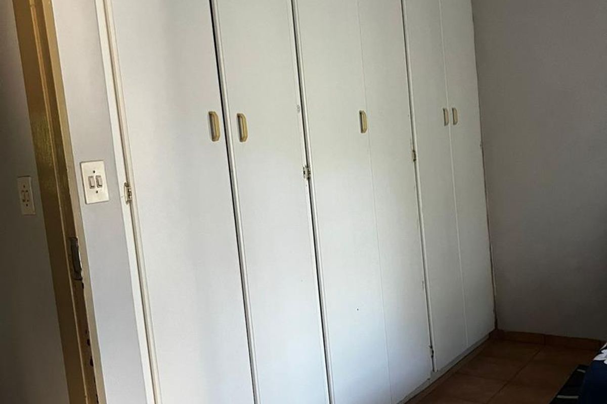 A bedroom featuring floor-to-ceiling built-in cupboards with white finish and tiled flooring.
