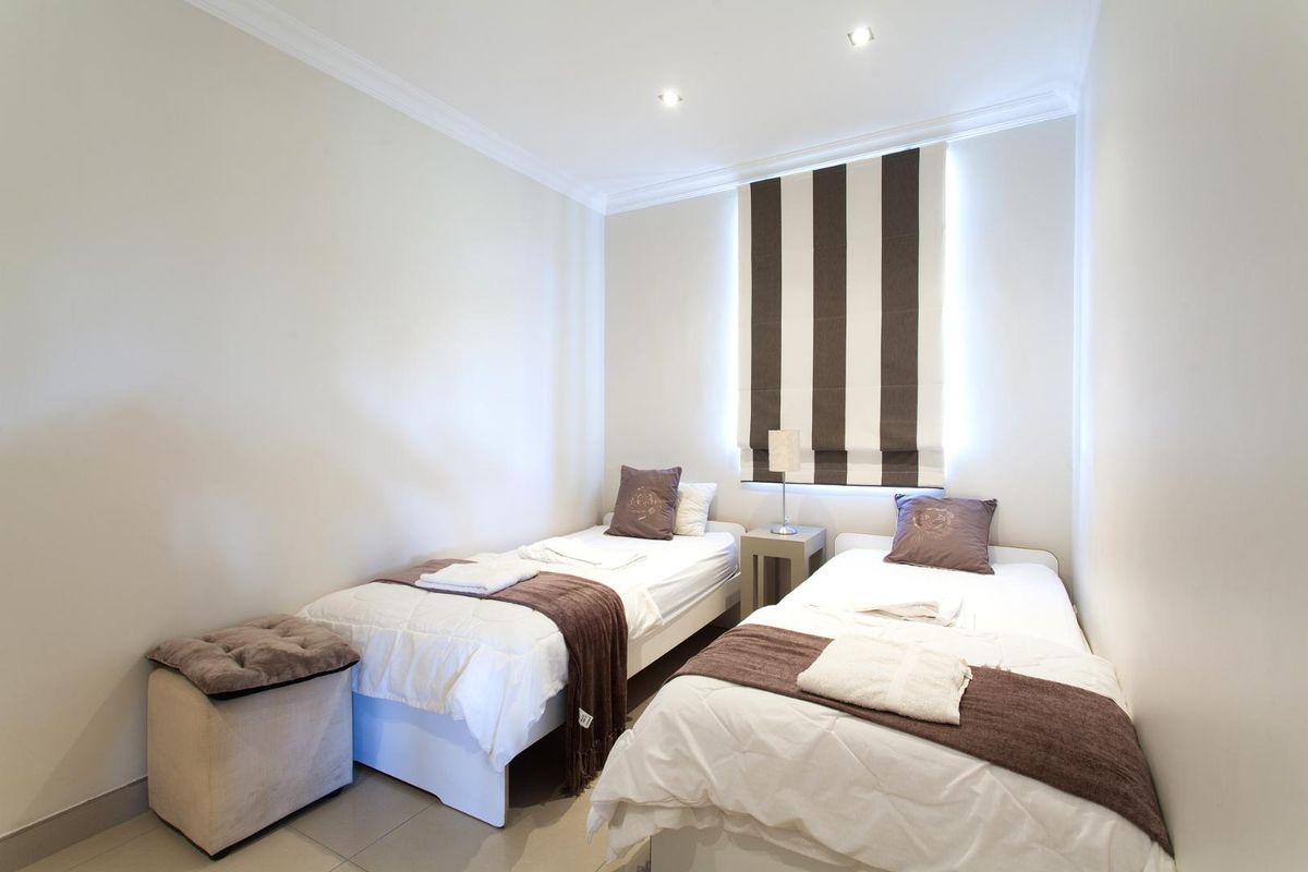 A well-maintained bedroom featuring neutral walls, recessed ceiling lighting, and a window with a fitted striped roman blind.