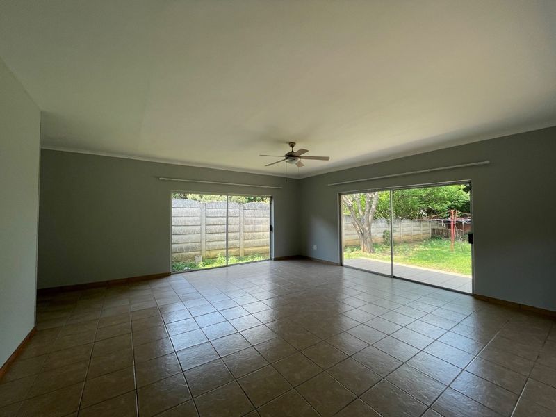 Spacious, empty living area featuring neutral tiled flooring, a ceiling fan, and large sliding glass doors providing direct access to the rear garden.