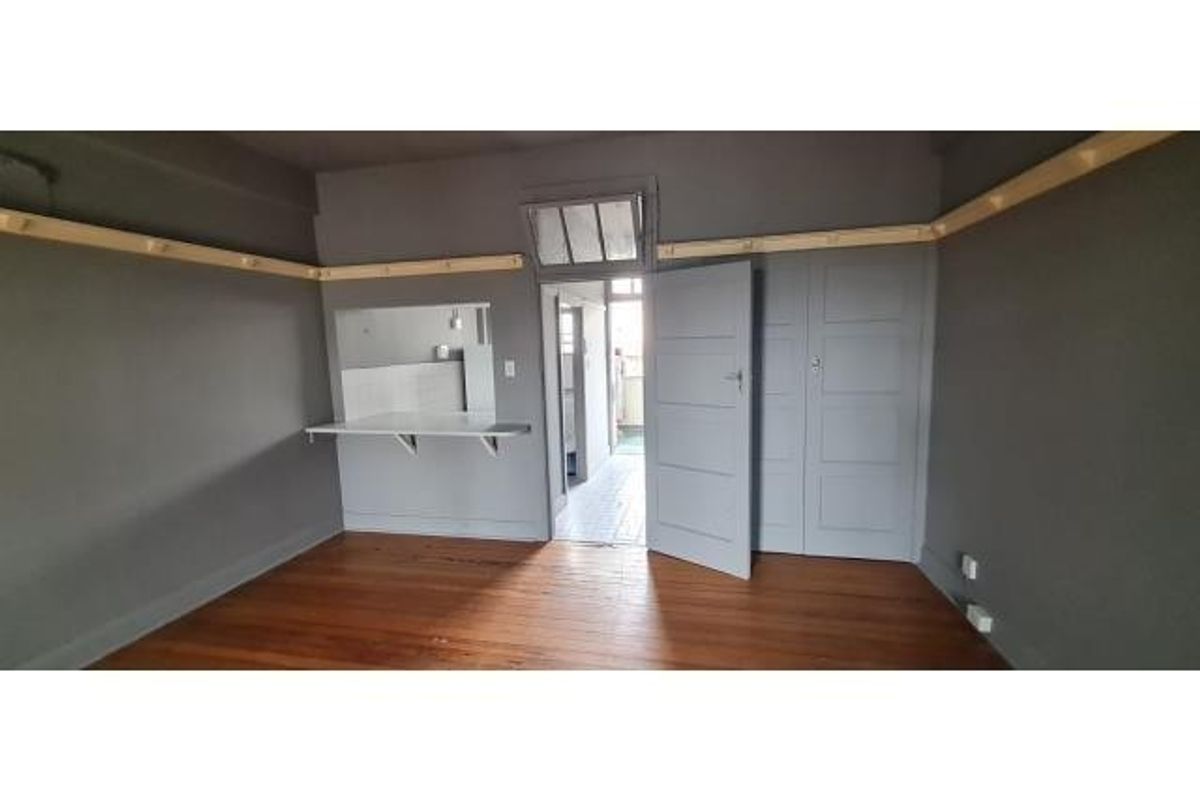 An empty living room featuring original hardwood flooring, built-in storage cabinetry, and a convenient serving hatch connecting to the adjacent kitchen area.