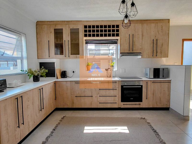 Modern kitchen featuring light wood-finish cabinetry, integrated oven and hob, ample counter space, and tiled flooring with natural light.