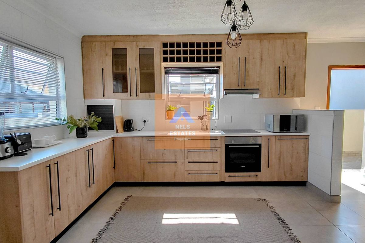 Modern kitchen featuring light wood-finish cabinetry, integrated oven and hob, ample counter space, and tiled flooring with natural light.
