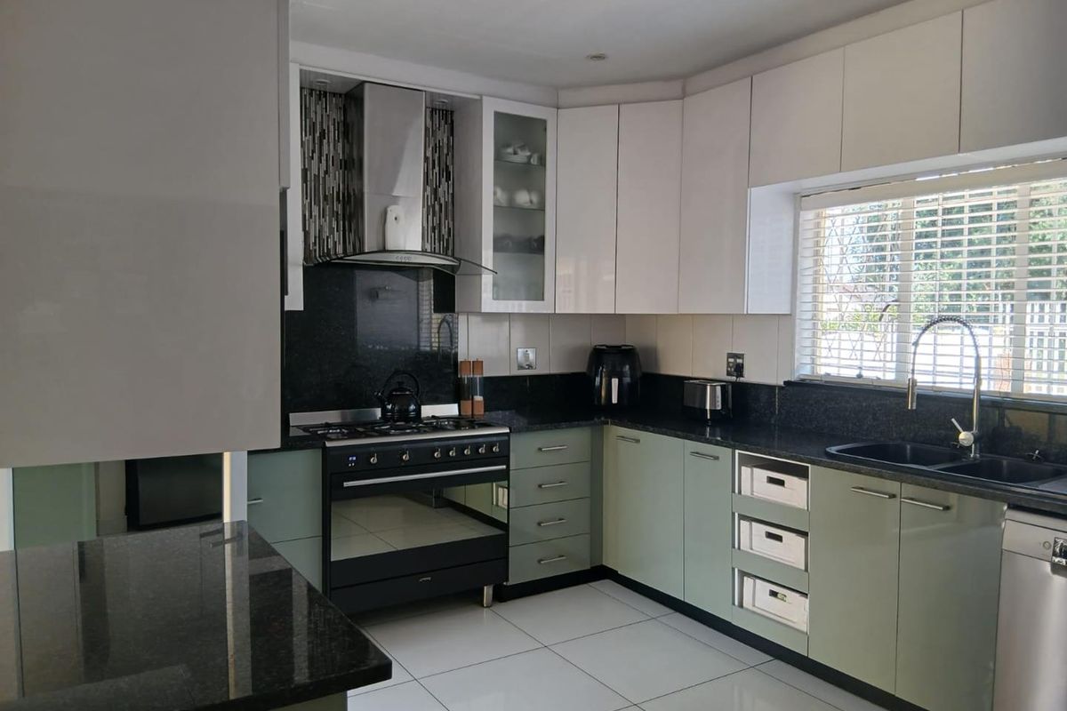 Modern kitchen featuring sleek cabinetry, granite countertops, a gas stove with extractor fan, and tiled flooring with ample natural light.