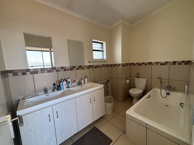 A functional bathroom featuring a double vanity with built-in cabinetry, a standard toilet, and a bathtub with tiled surround and splashback.