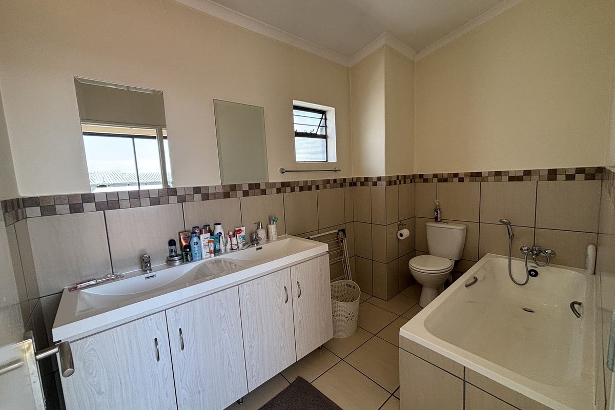 A functional bathroom featuring a double vanity with built-in cabinetry, a standard toilet, and a bathtub with tiled surround and splashback.