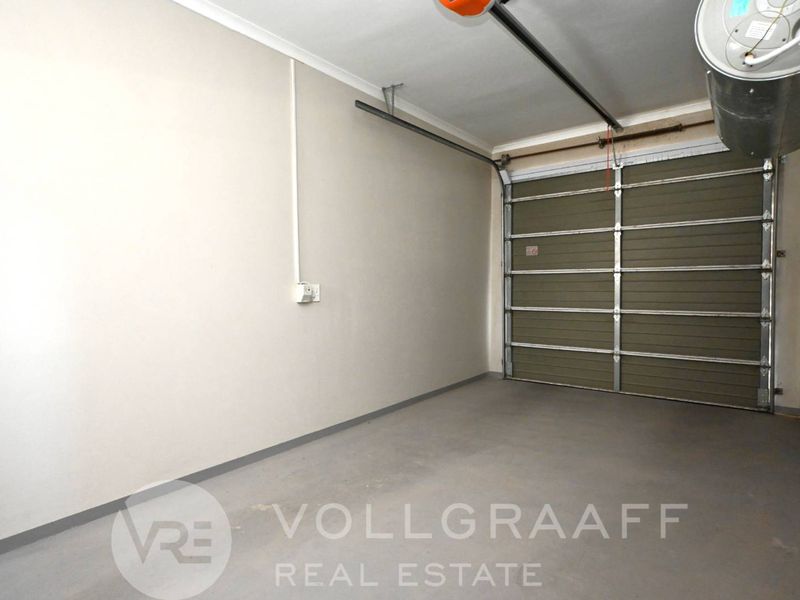 A clean and functional single garage featuring a sectional door, automated motor, and an installed geyser.