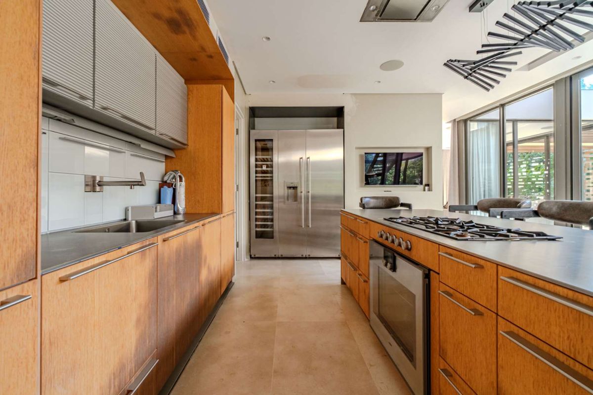 Modern kitchen featuring wood cabinetry, stone countertops, integrated stainless steel appliances, a central island with a gas cooktop, and built-in wine refrigeration.