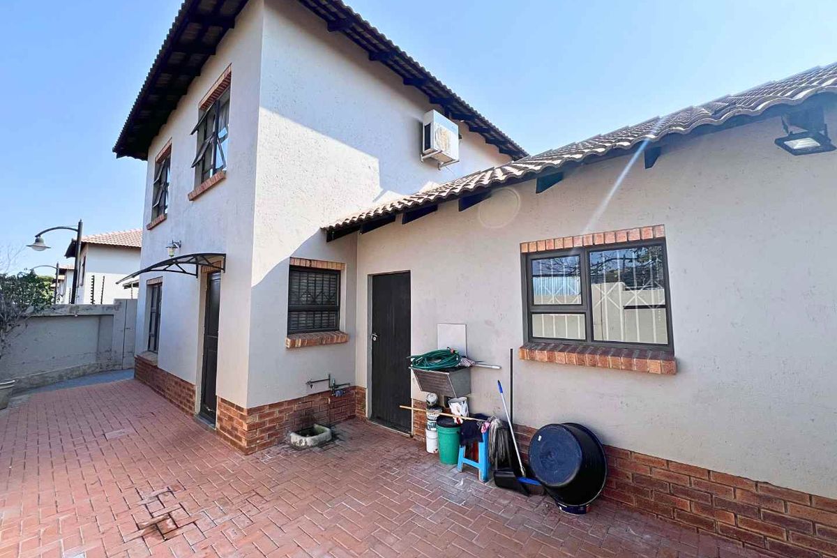 Rear exterior view of the townhouse featuring brick paving, a tiled roof, and an external utility sink area.