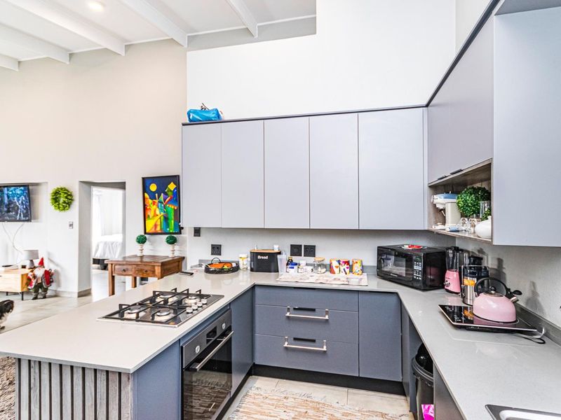 Modern kitchen featuring sleek grey cabinetry, stone countertops, integrated gas cooktop, built-in oven, and high ceilings with exposed beams.