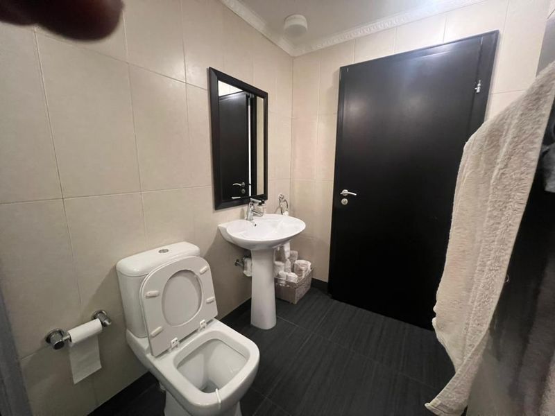 A functional bathroom featuring a pedestal basin, toilet, and neutral wall tiling with dark floor tiles.