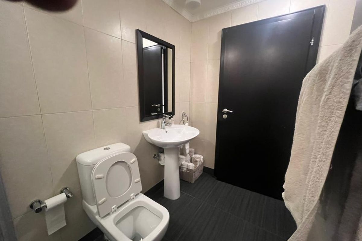 A functional bathroom featuring a pedestal basin, toilet, and neutral wall tiling with dark floor tiles.