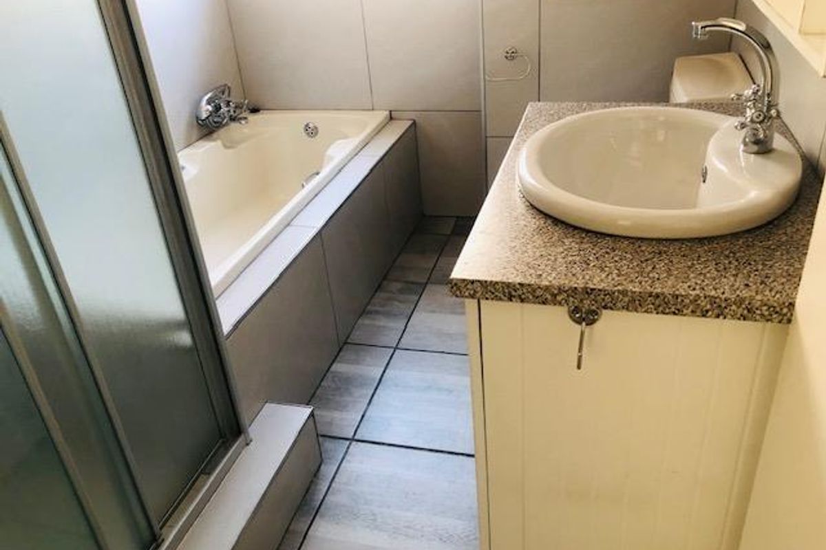A functional bathroom featuring a built-in bathtub, a separate shower enclosure, and a vanity unit with a countertop basin.