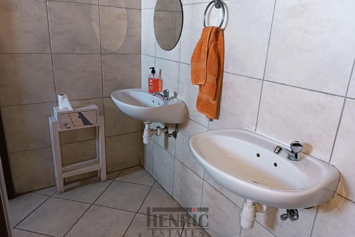 A functional office bathroom featuring dual wall-mounted ceramic washbasins with chrome fixtures and neutral floor-to-ceiling wall tiling.