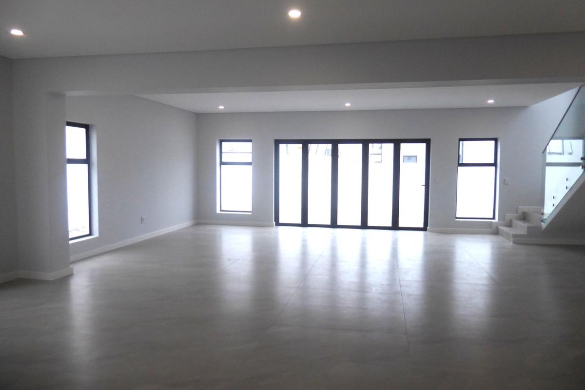 A spacious, modern open-plan living area featuring large format floor tiles, recessed lighting, and aluminium stacker doors leading to the exterior.
