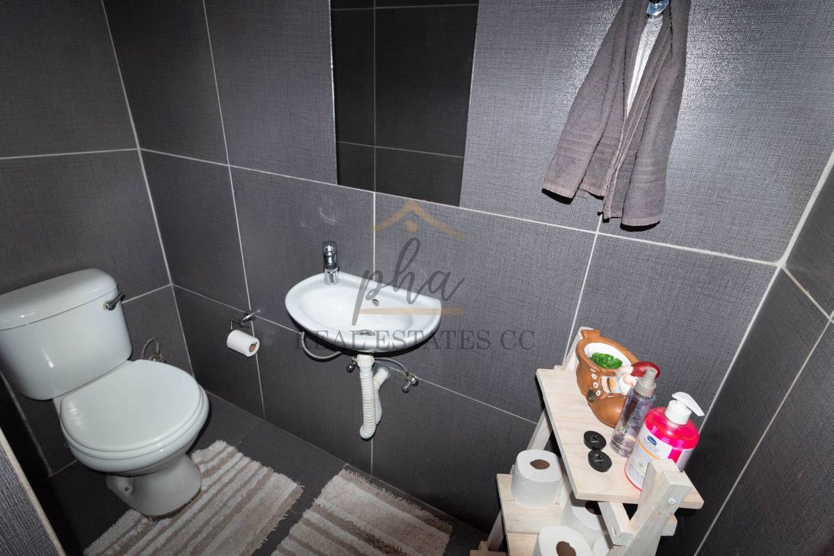 A compact guest bathroom featuring dark grey wall tiling, a white ceramic toilet, and a wall-mounted basin.