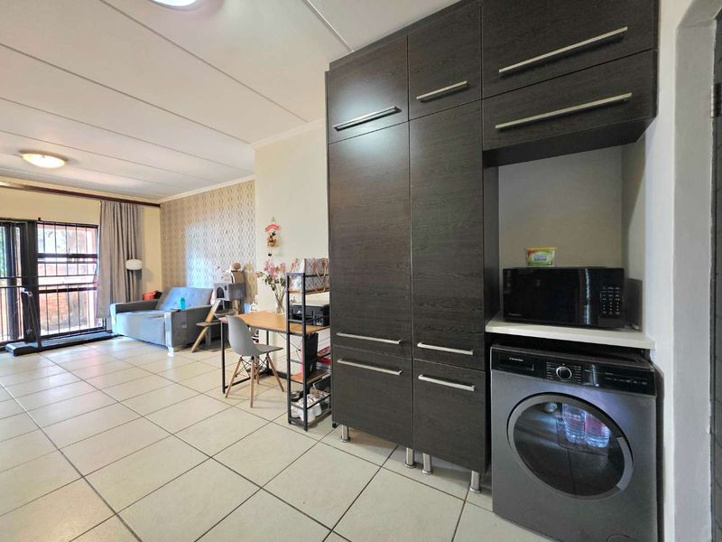 Open plan living area featuring tiled flooring and a modern dark wood built-in cabinetry unit with integrated laundry appliance space.