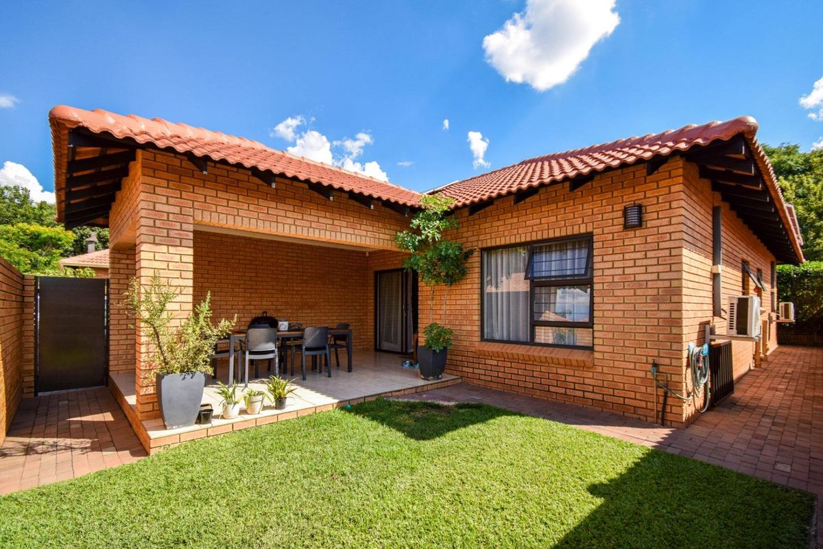 A well-maintained rear exterior view featuring a covered patio with tiled flooring, face-brick walls, terracotta roof tiles, and a small private garden area.