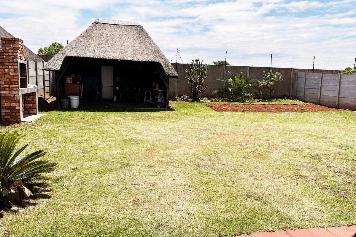 Spacious rear garden featuring a thatched lapa with a built-in brick braai, enclosed by perimeter walling with electric fencing.