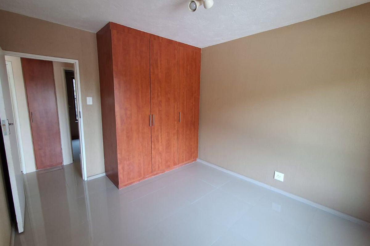 A clean, empty bedroom featuring neutral wall tones, polished tile flooring, and ample built-in cupboard storage.