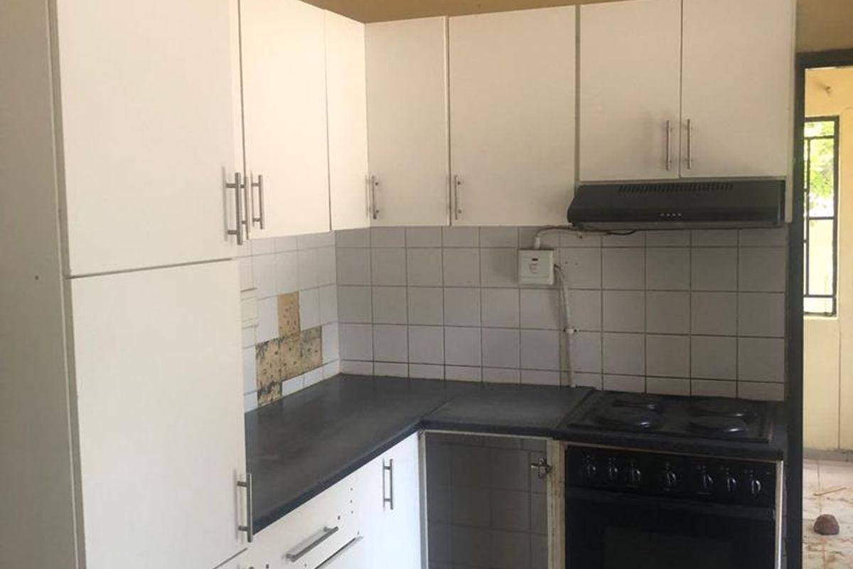 A compact kitchen featuring white cabinetry, a built-in oven with extractor fan, and tiled flooring, requiring some maintenance and finishing touches.