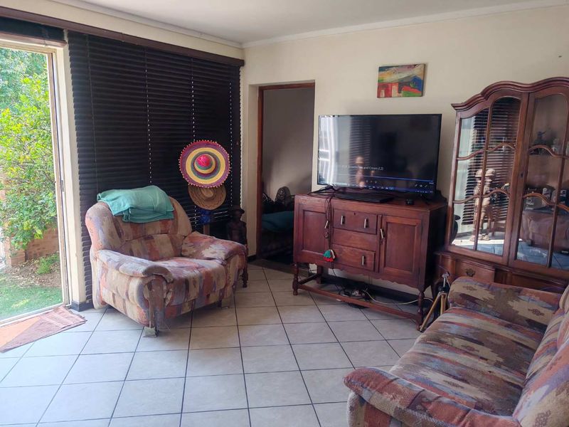 A living room featuring tiled flooring and a sliding glass door with venetian blinds, providing direct access to the outdoor area.