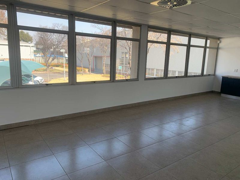 A bright, open-plan office space featuring large windows, tiled flooring, and a suspended ceiling, offering a clean and functional workspace.