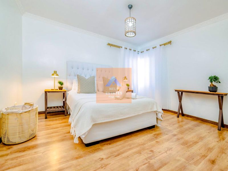 A bright and well-maintained bedroom featuring laminate flooring, crown molding, and a central pendant light fixture.
