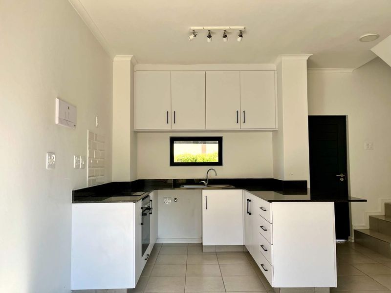 A clean, modern kitchen featuring white cabinetry, dark granite countertops, built-in oven, and tiled flooring in an open-plan layout.