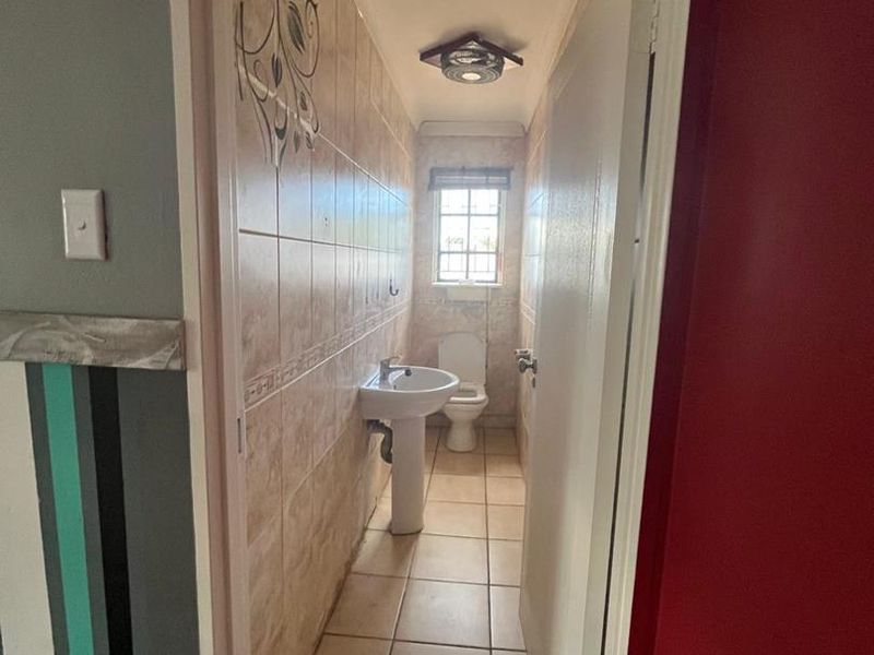 A narrow guest bathroom featuring a pedestal basin, toilet, and tiled finishes, requiring cosmetic updates to improve its dated appearance.