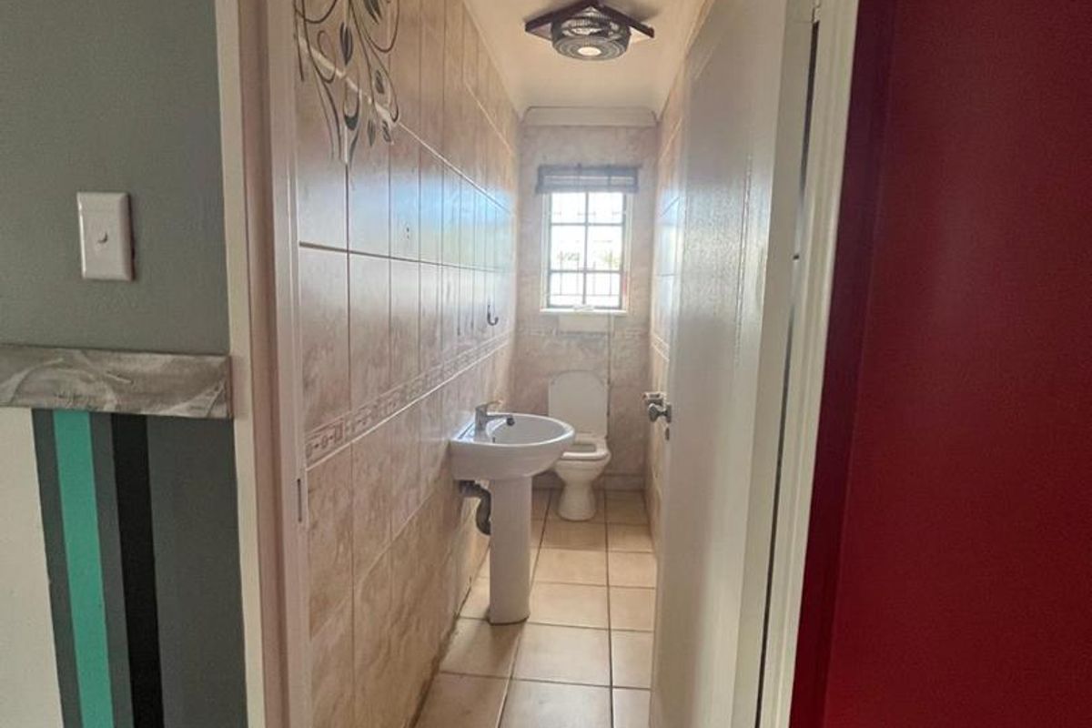 A narrow guest bathroom featuring a pedestal basin, toilet, and tiled finishes, requiring cosmetic updates to improve its dated appearance.
