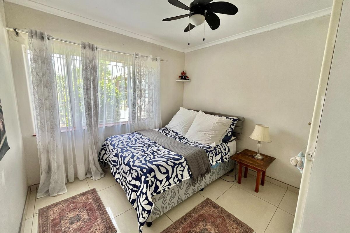 A functional bedroom featuring tiled flooring, a ceiling fan, and security burglar bars on the window.