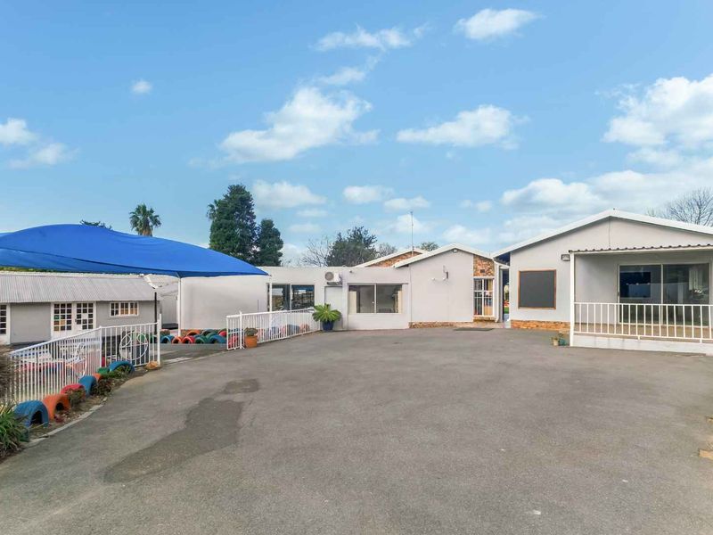 Spacious rear exterior area featuring an asphalt driveway, metal safety railings, and a large blue shade sail covering a portion of the yard.
