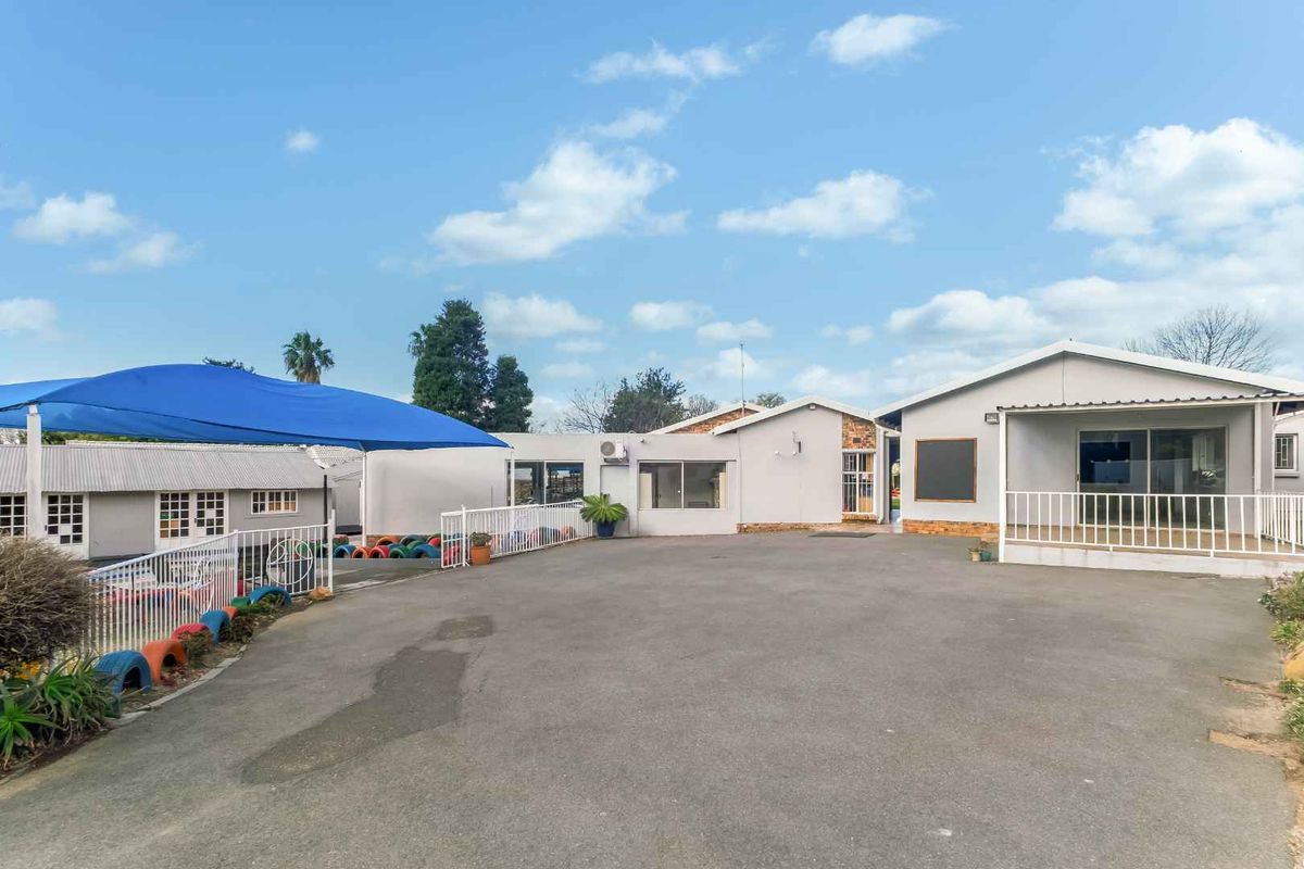 Spacious rear exterior area featuring an asphalt driveway, metal safety railings, and a large blue shade sail covering a portion of the yard.