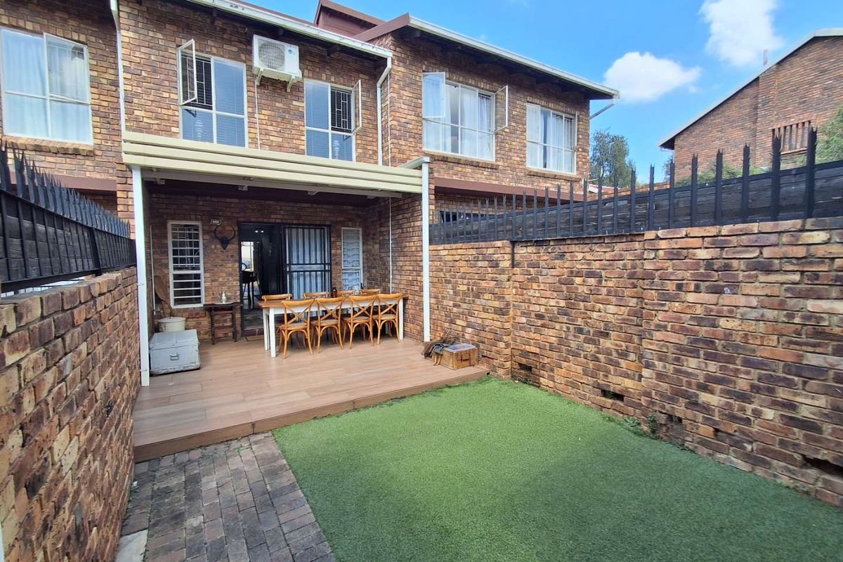 A private rear courtyard featuring a timber deck, artificial lawn, and a covered patio area, enclosed by brick boundary walls.