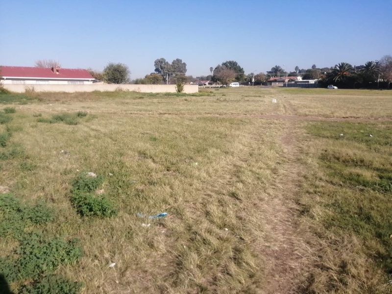 A vacant residential plot of land featuring open grass and a perimeter boundary wall, suitable for future development.