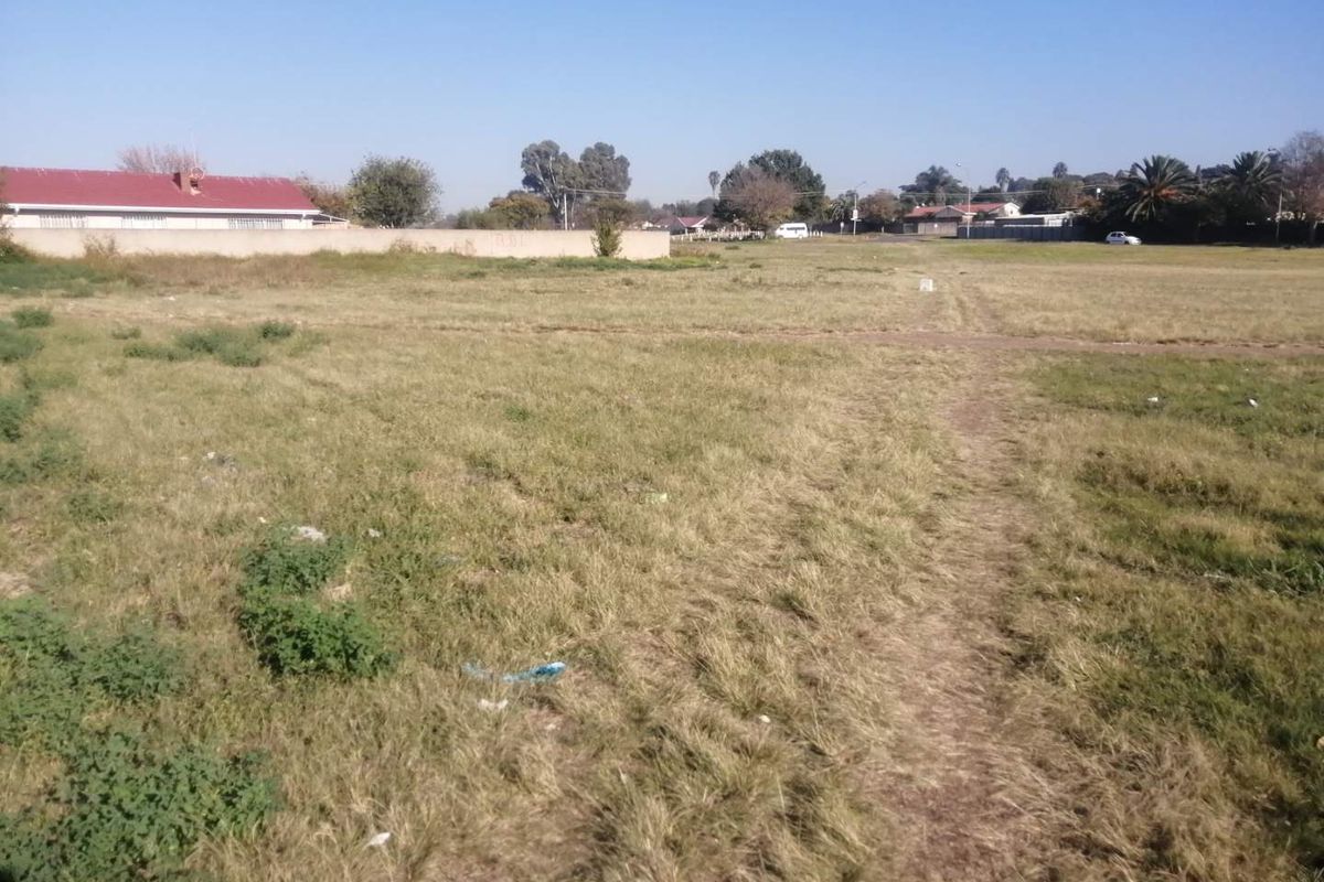 A vacant residential plot of land featuring open grass and a perimeter boundary wall, suitable for future development.