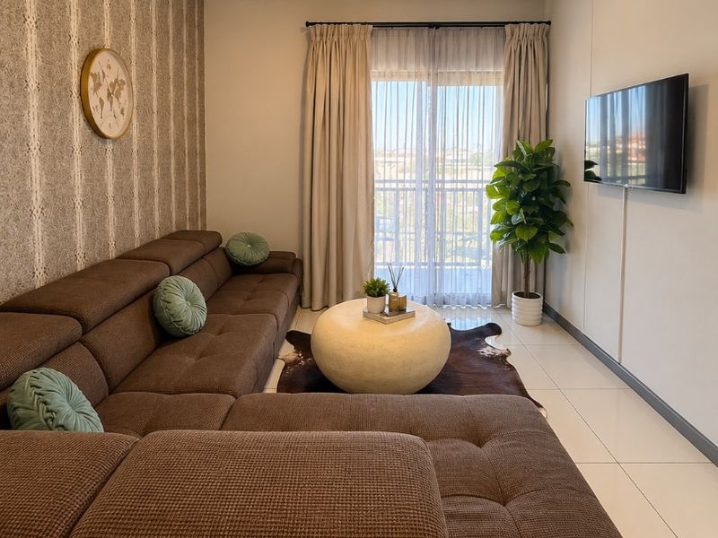 A well-maintained living room featuring tiled flooring, a wall-mounted television, and a sliding glass door providing access to a balcony.