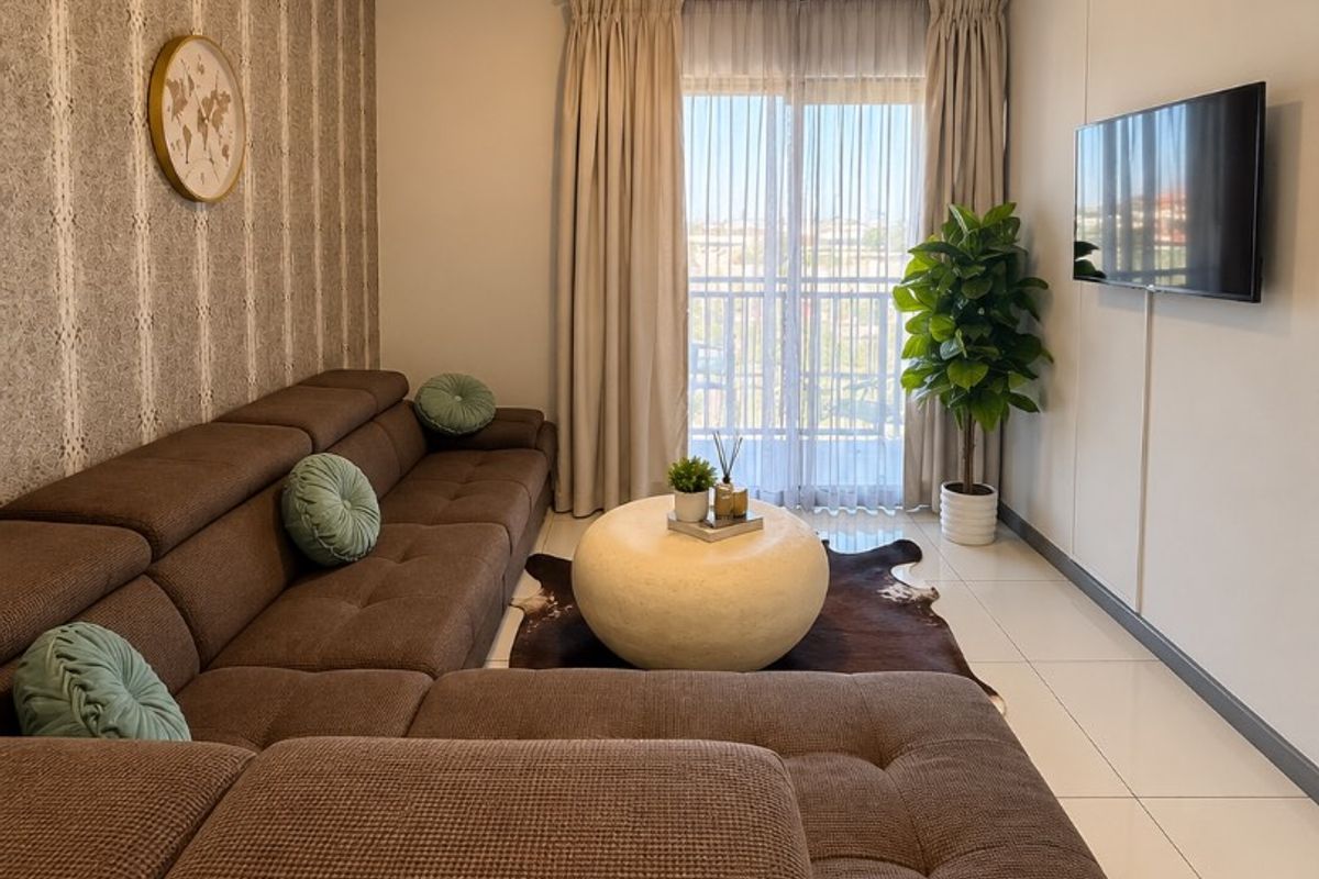 A well-maintained living room featuring tiled flooring, a wall-mounted television, and a sliding glass door providing access to a balcony.