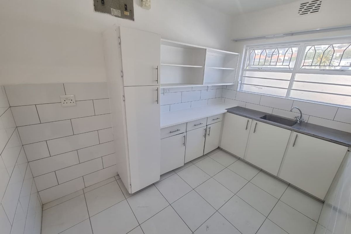 A functional, empty kitchen featuring white cabinetry, subway tile backsplash, laminate countertops, and ceramic floor tiles with a window overlooking the exterior.