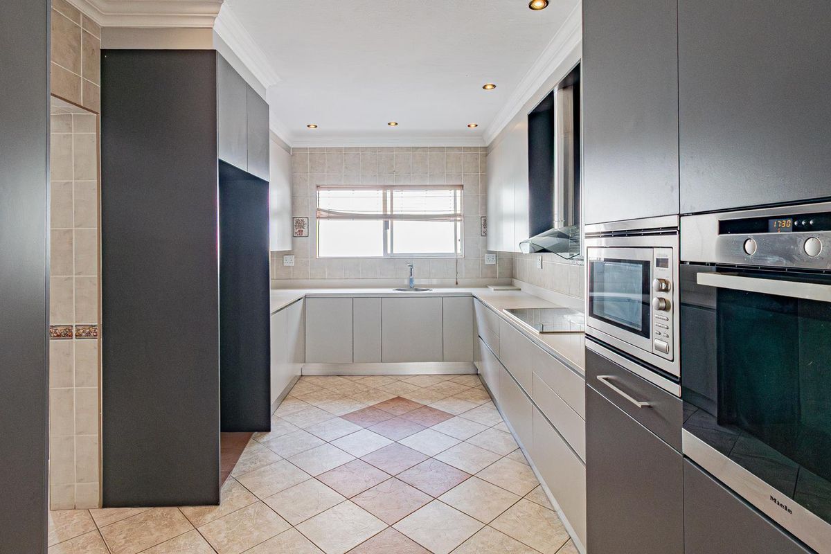 A modern, well-maintained kitchen featuring sleek grey cabinetry, integrated appliances, tiled flooring, and ample counter space with a functional layout.