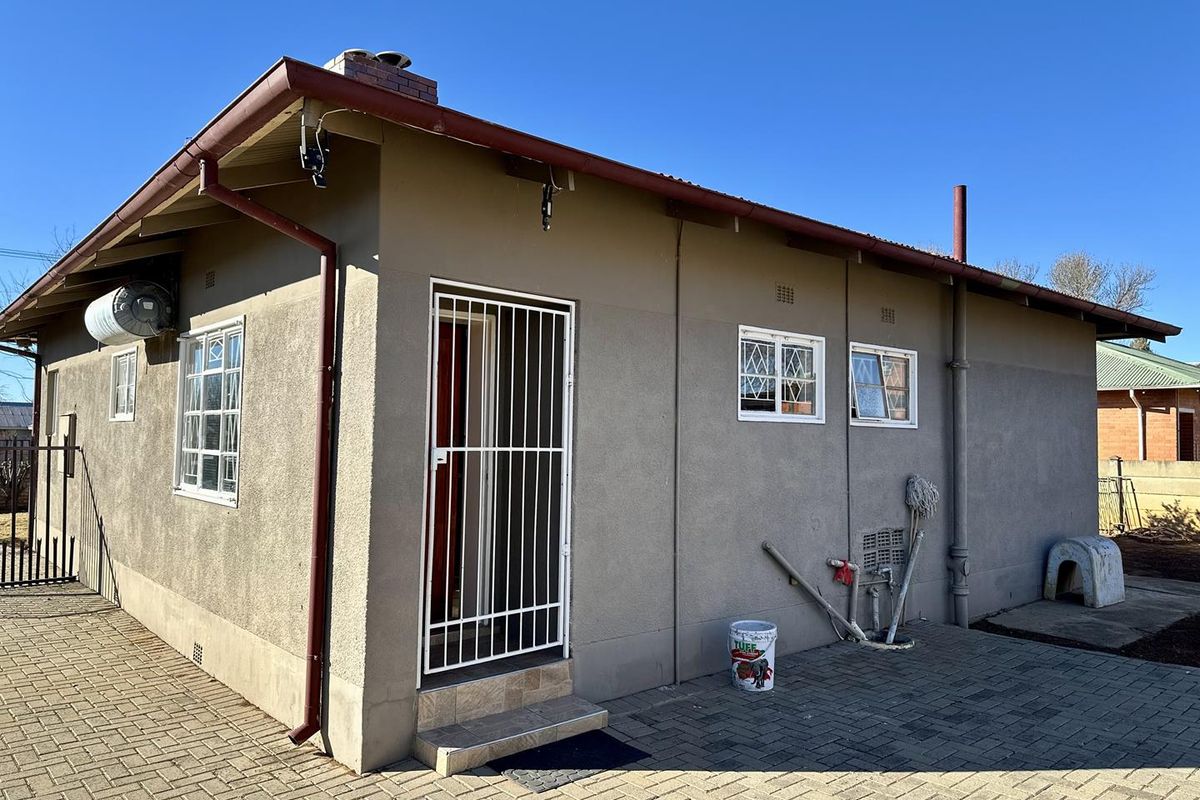 Rear exterior view of the house featuring a paved patio area, security gate, and burglar bars on the windows.