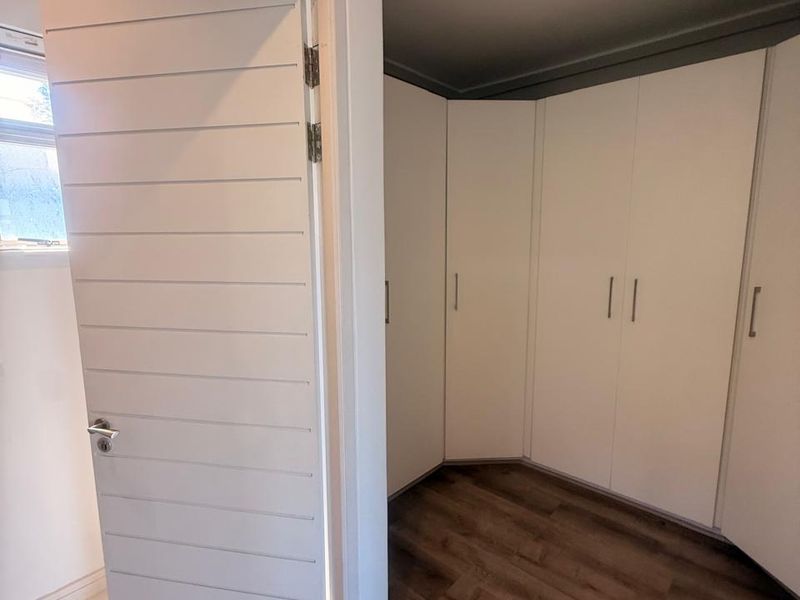 A clean, empty bedroom featuring modern built-in cupboards, warm laminate flooring, and recessed downlighting, offering a neutral space ready for personalization.